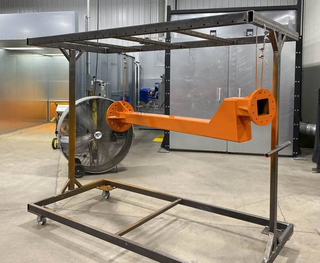 In a warehouse in Michigan, a large orange machine for powder coating pretreatment sits on a rack.