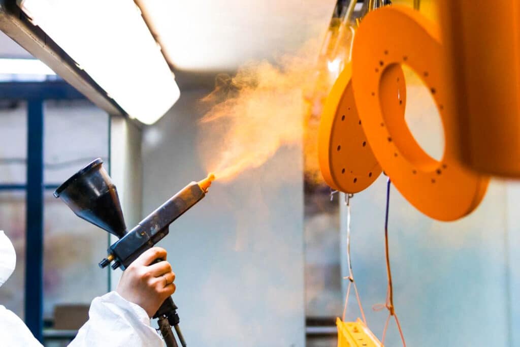 A person applying Liberty Powder Coating on a metal object for packaging.