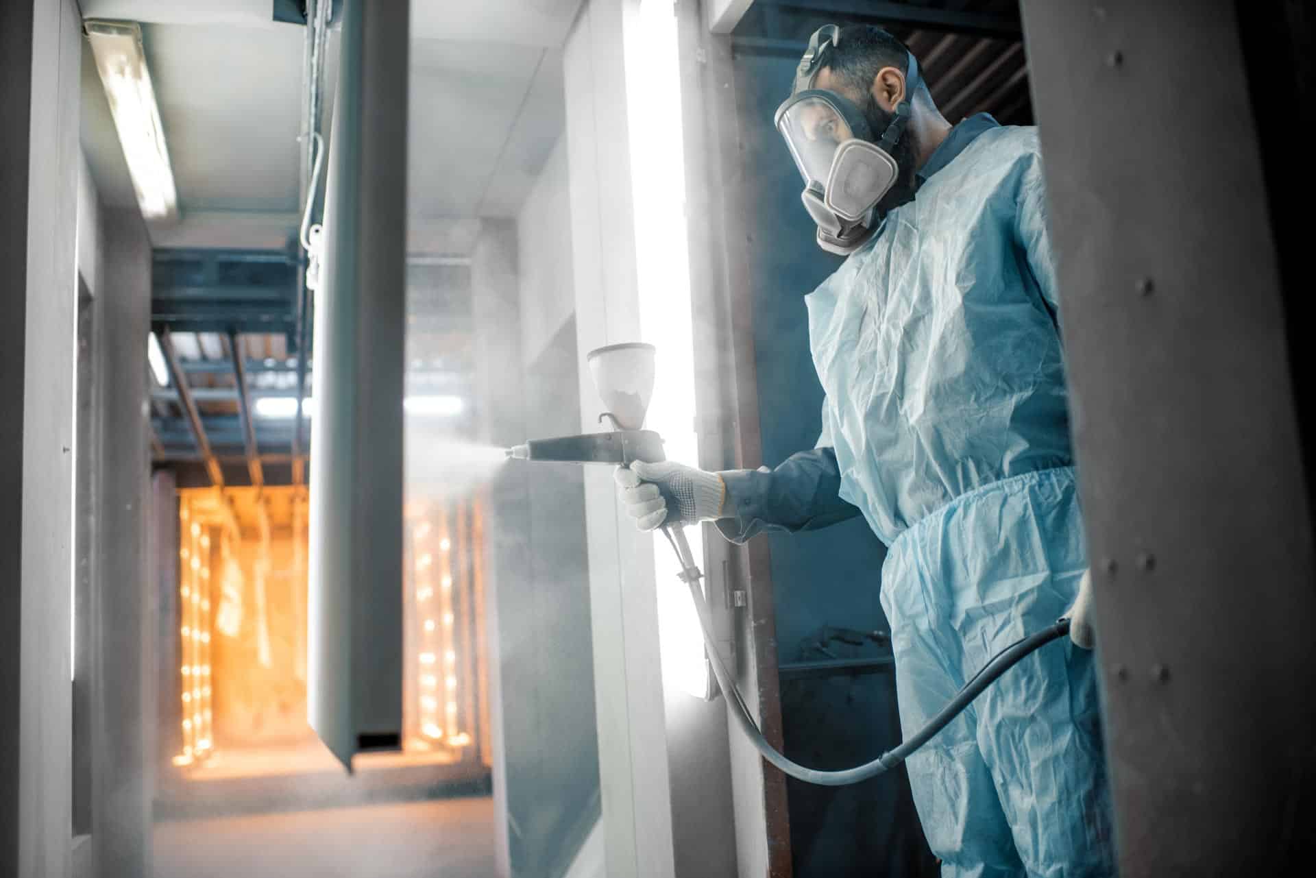 A man in a protective suit pretreatment spraying paint on a wall for powder coating.