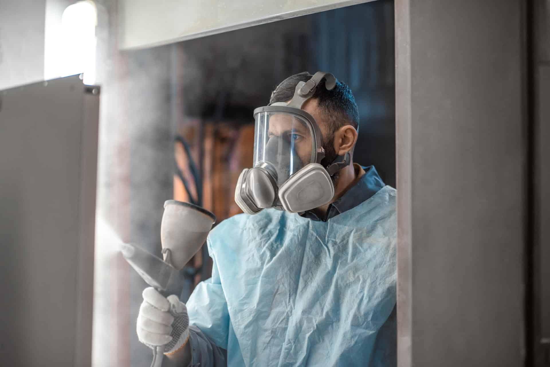 A man in a protective suit applying Liberty Powder Coating to a door in Michigan.