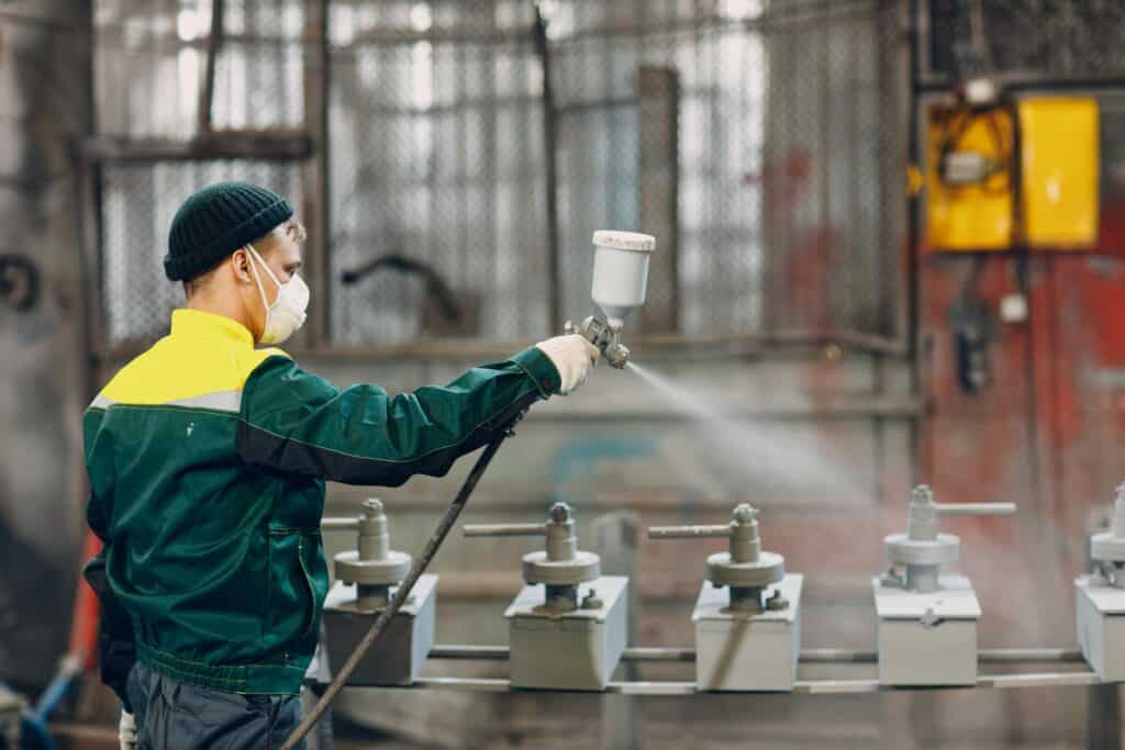 A worker from Liberty Powder Coating spraying paint on a machine in a factory.