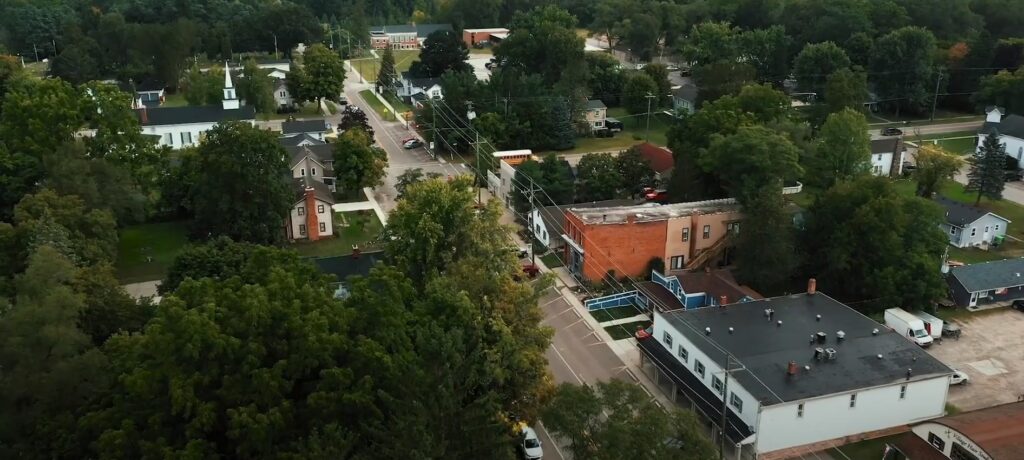 Aerial view of a small town in Michigan with residential and commercial buildings surrounded by greenery.