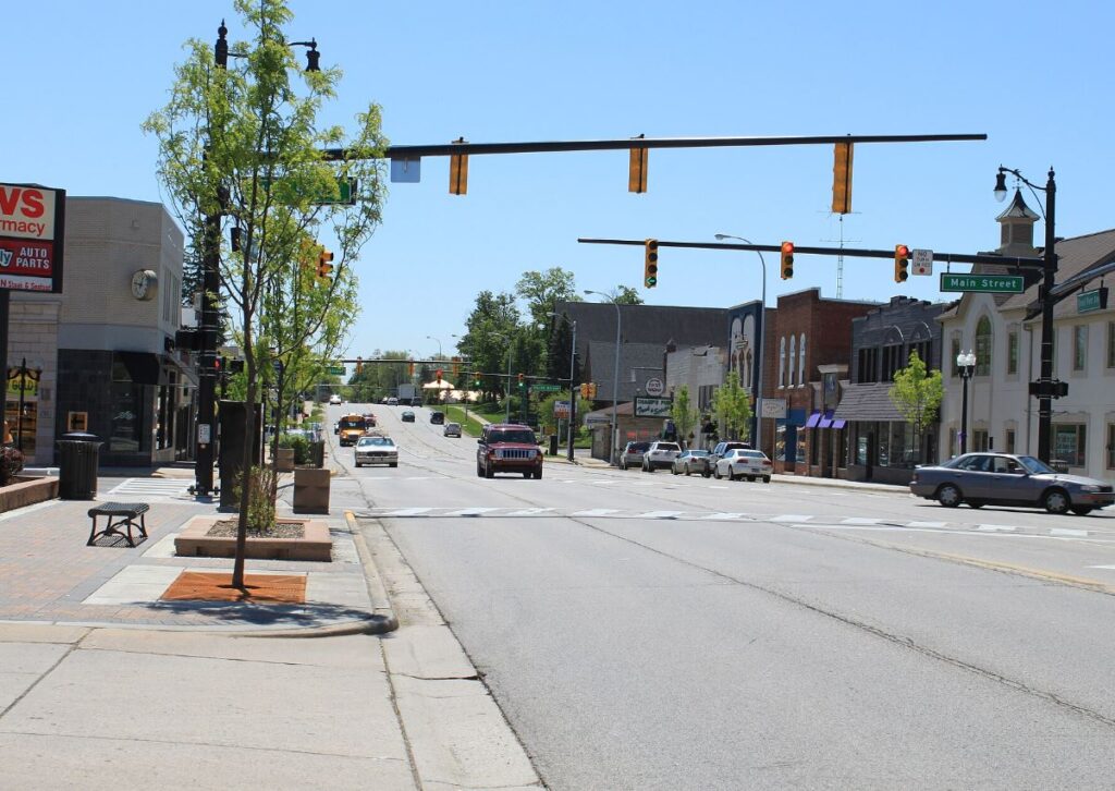 Sunny day on a suburban street in Michigan with traffic lights and roadside businesses specializing in powder coating.