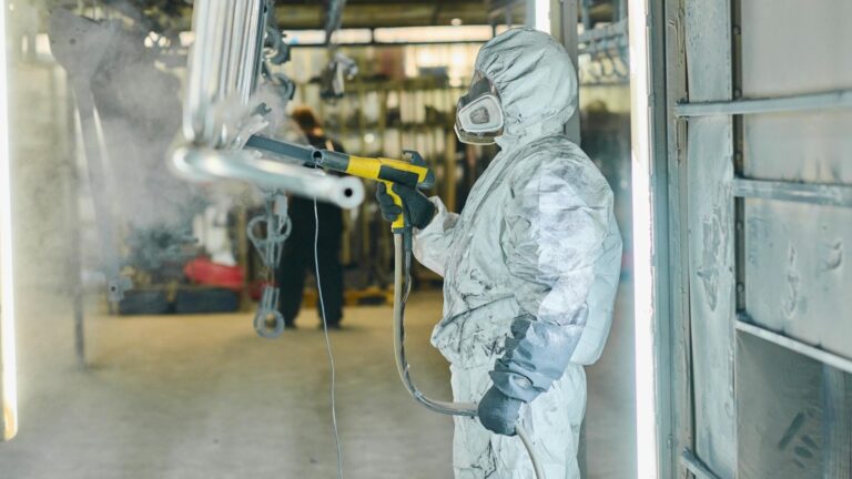 custom powder coating in michigan technician spraying metal part with powder coat fabrication